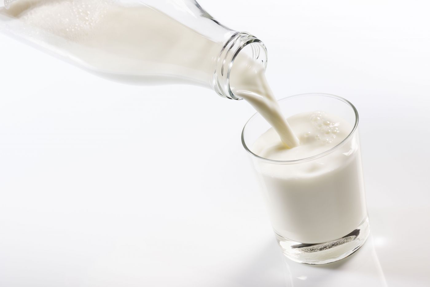 Milch wird aus der Milch-Glasflasche in ein Glas gelehrt