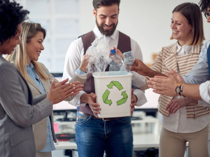 Fünf Menschen stehen um einen Recycling Mistkübel und lachen