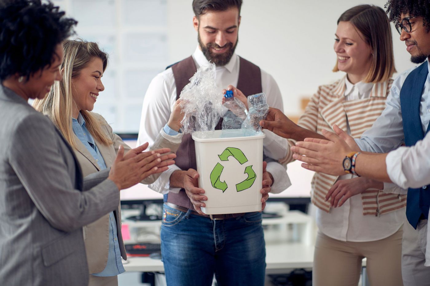 Fünf Menschen stehen um einen Recycling Mistkübel und lachen