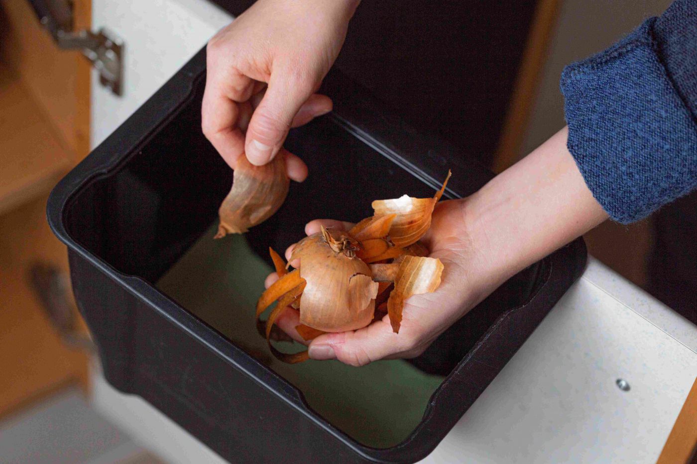 Hände geben Zwiebelschalen in den Komposmüll