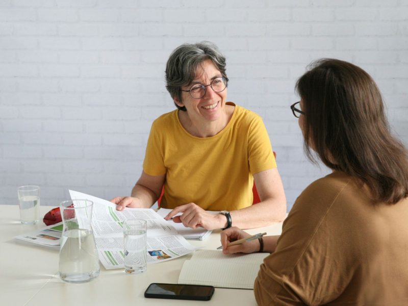 Zwei Frauen sitzen an einem Tisch und führen ein Gespräch.