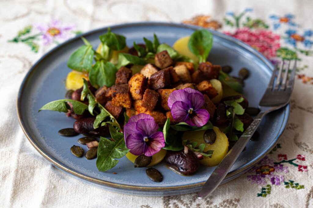 Löwenzahnsalat mit Tofu und Käferbohnen serviert am blauen Teller