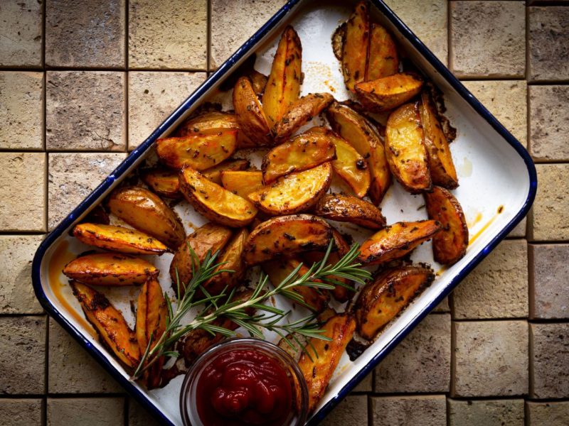 Potato Wedges in einer Auflaufform mit Rosmarin und Ketchup